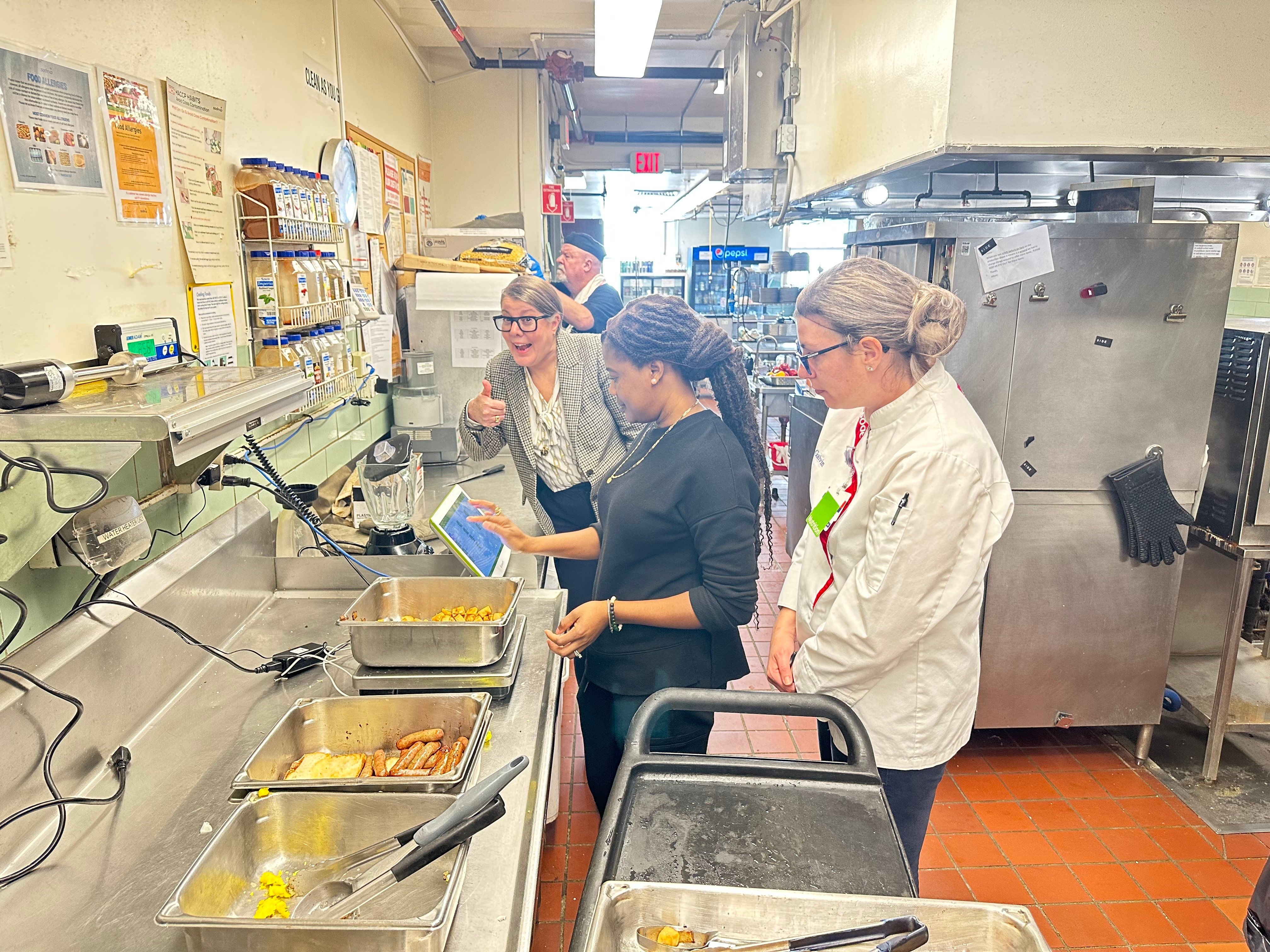 Team member logging leftover breakfast potatoes on a Leanpath tracker while a chef and manager look on