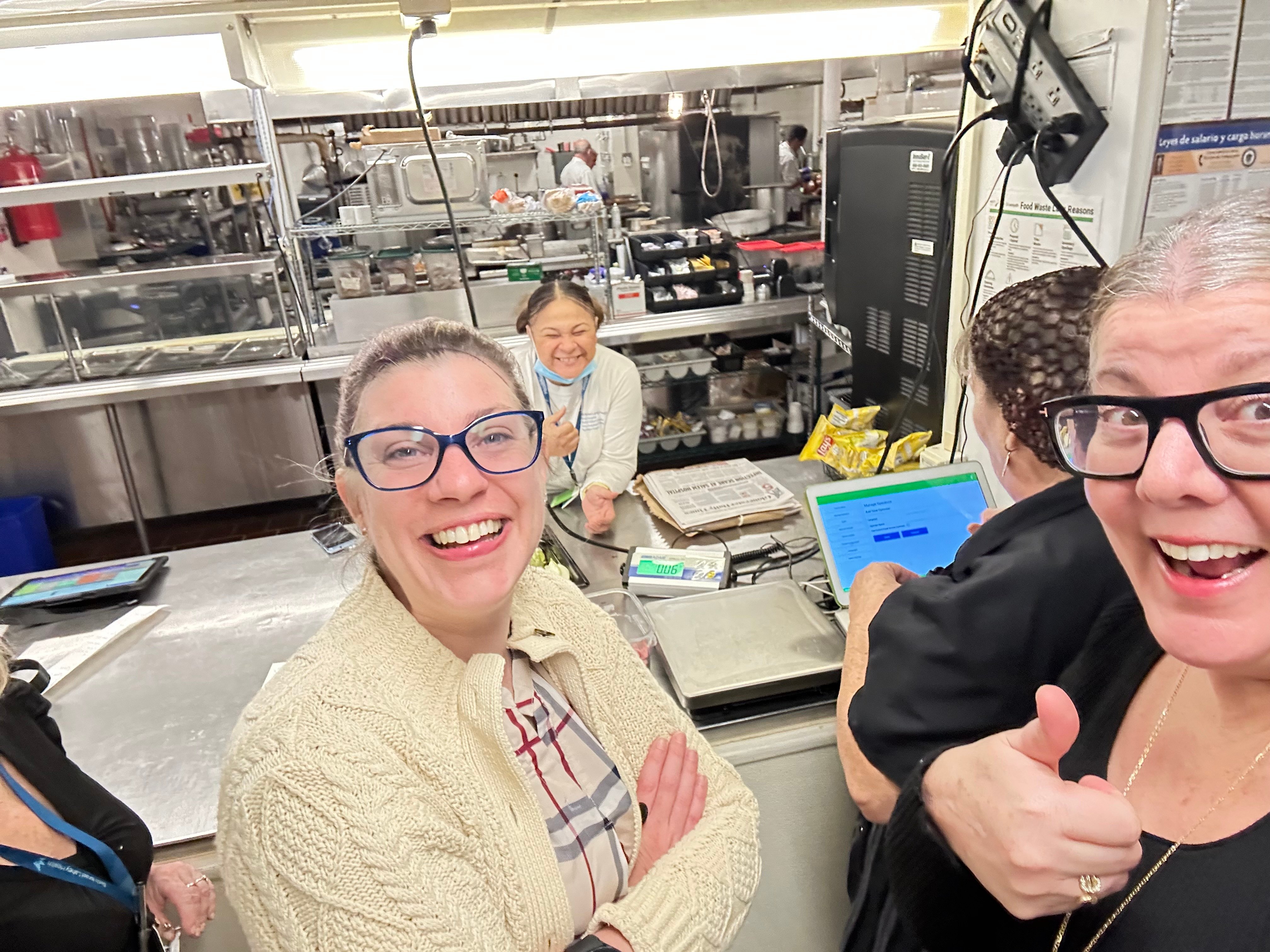 Smiling foodservice team giving a thumbs up beside a Leanpath tracker in a hospital kitchen